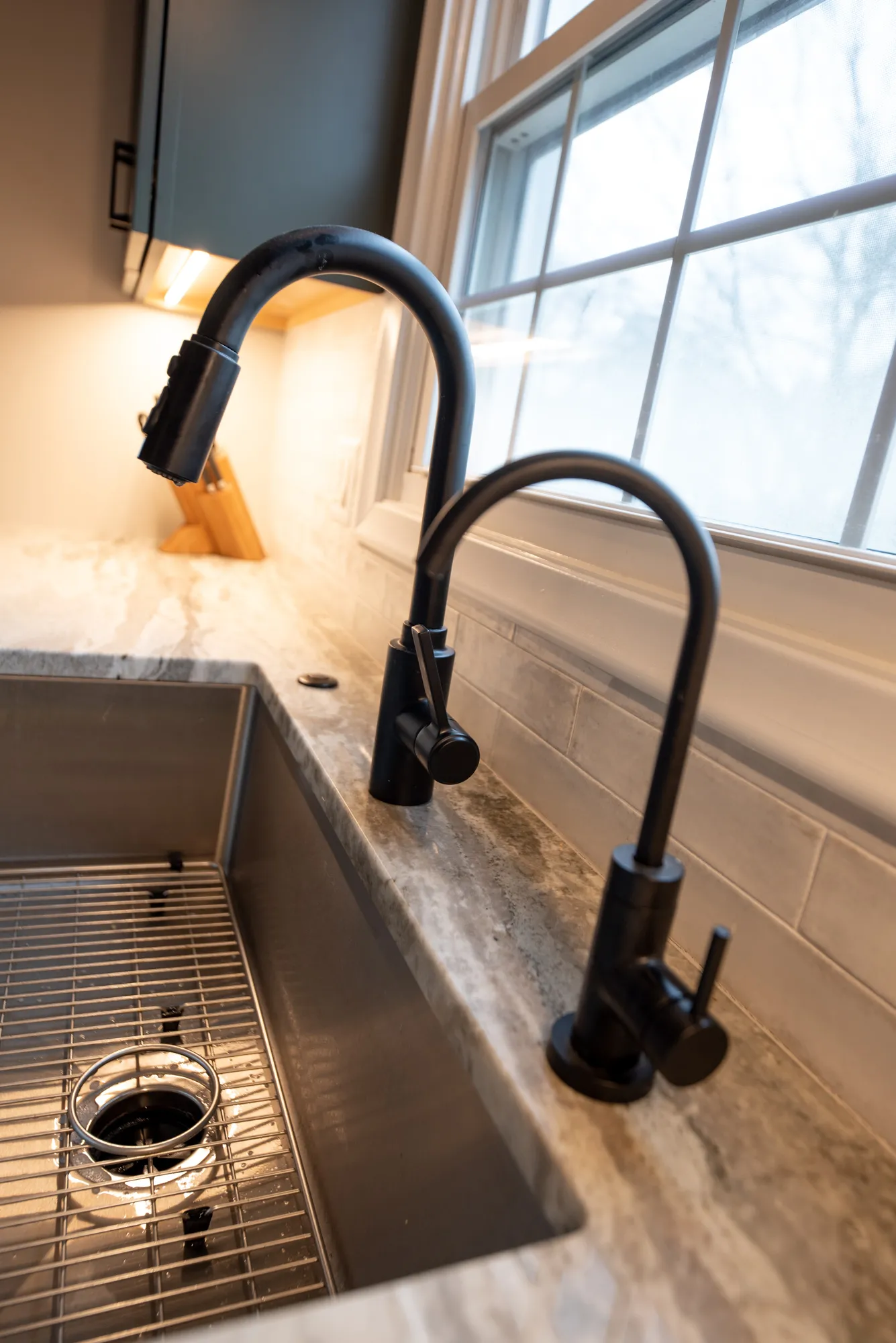 Modern kitchen sink featuring dual matte black faucets and a stainless steel basin with grey marble countertop