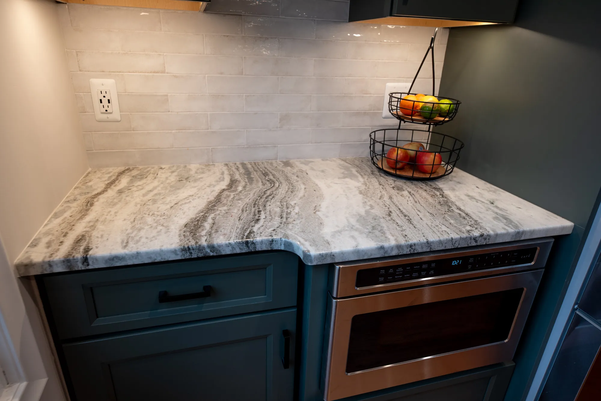 Modern kitchen featuring a sleek marble countertop with green cabinets and a wire fruit basket