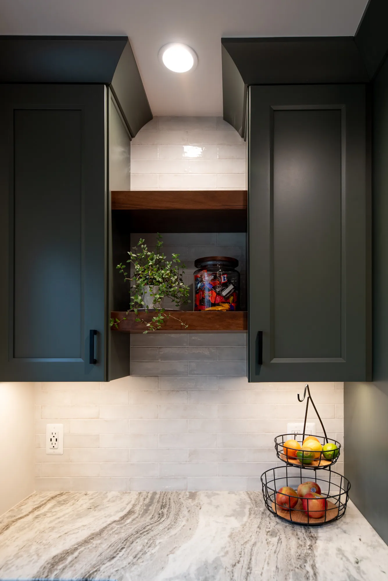 Contemporary kitchen corner with dark green cabinets, marble countertop, and decorative open shelving.