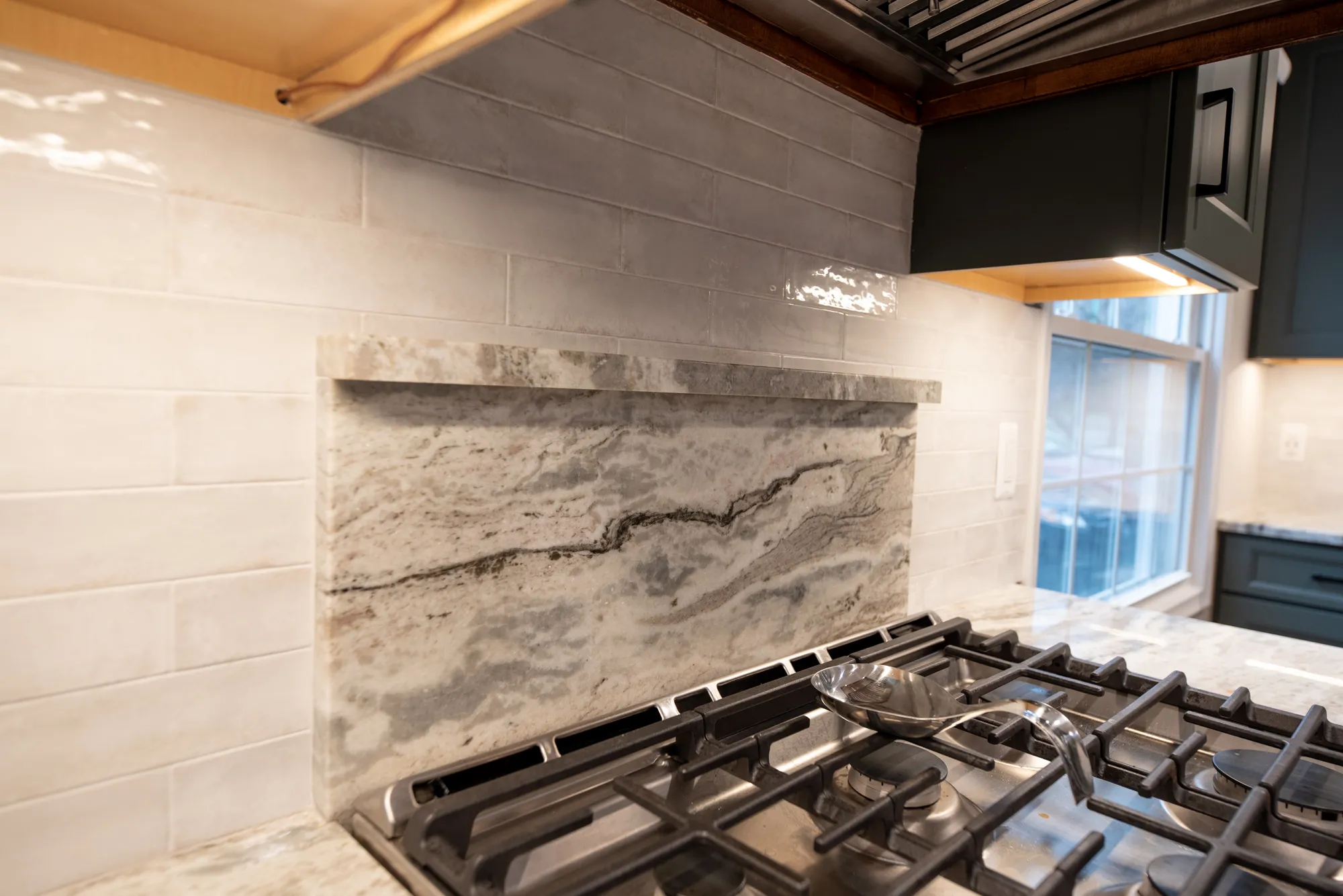 Modern kitchen featuring a stunning gray marble backsplash and stainless steel gas stove, emphasizing contemporary design elements.
