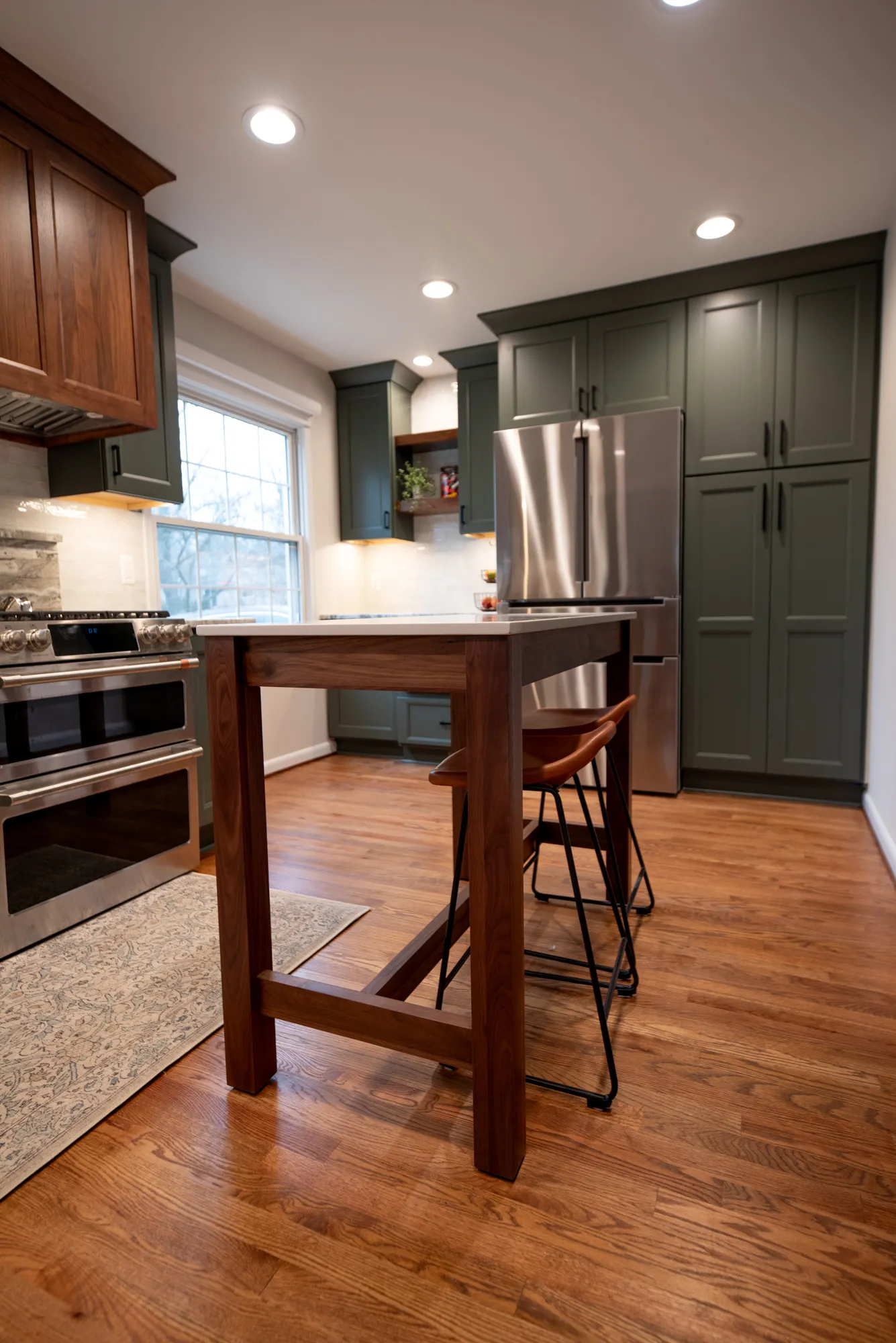 Modern kitchen featuring dark green cabinets, stainless steel appliances, and a wooden counter in a cozy setting