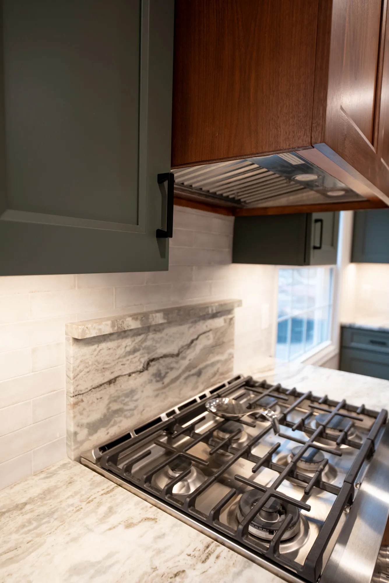 Modern kitchen with gray shaker cabinets and a sleek gas stove featuring a marble backsplash.