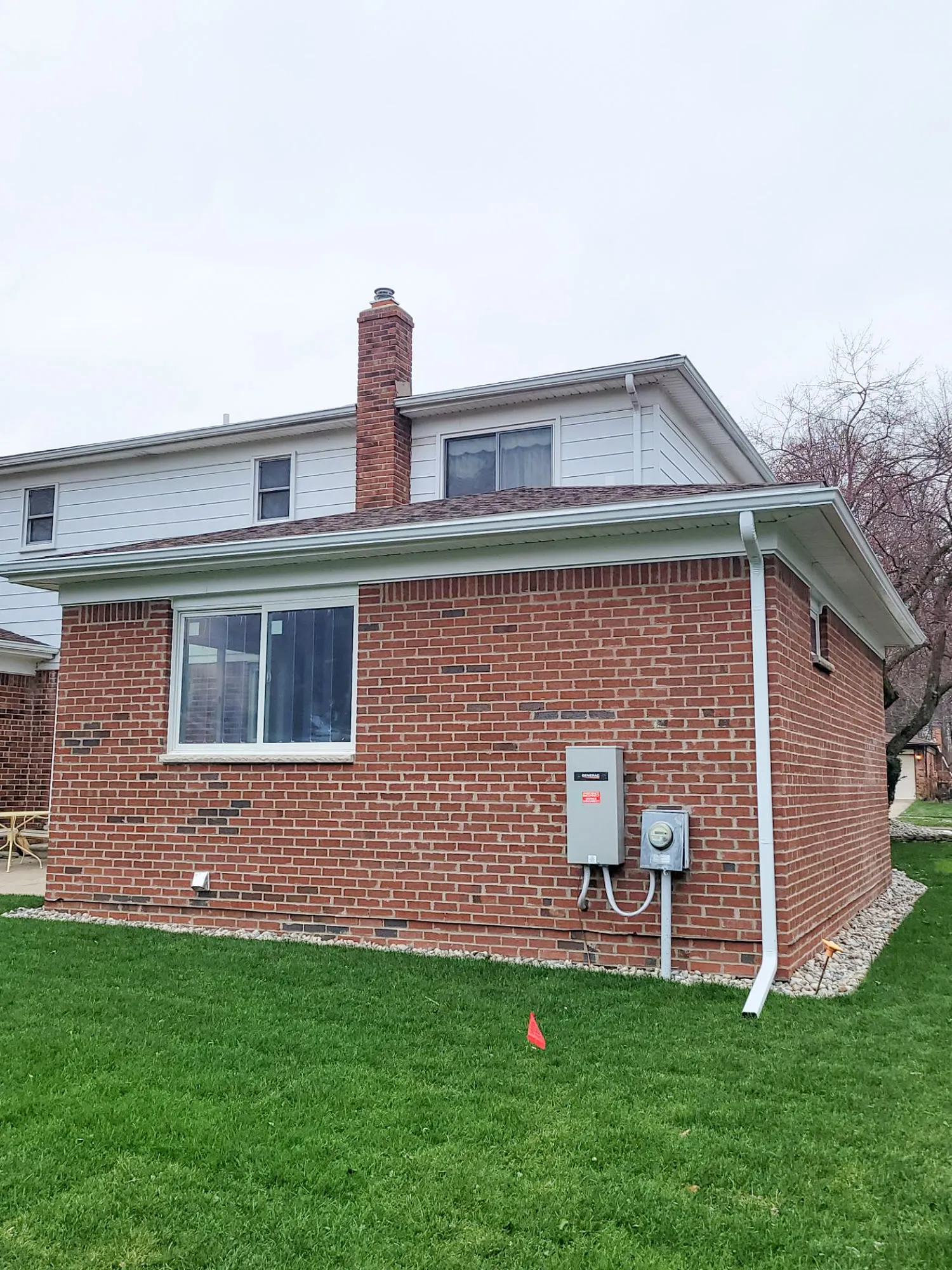 Exterior view of a two-story brick house with white siding and a green lawn in a suburban setting.
