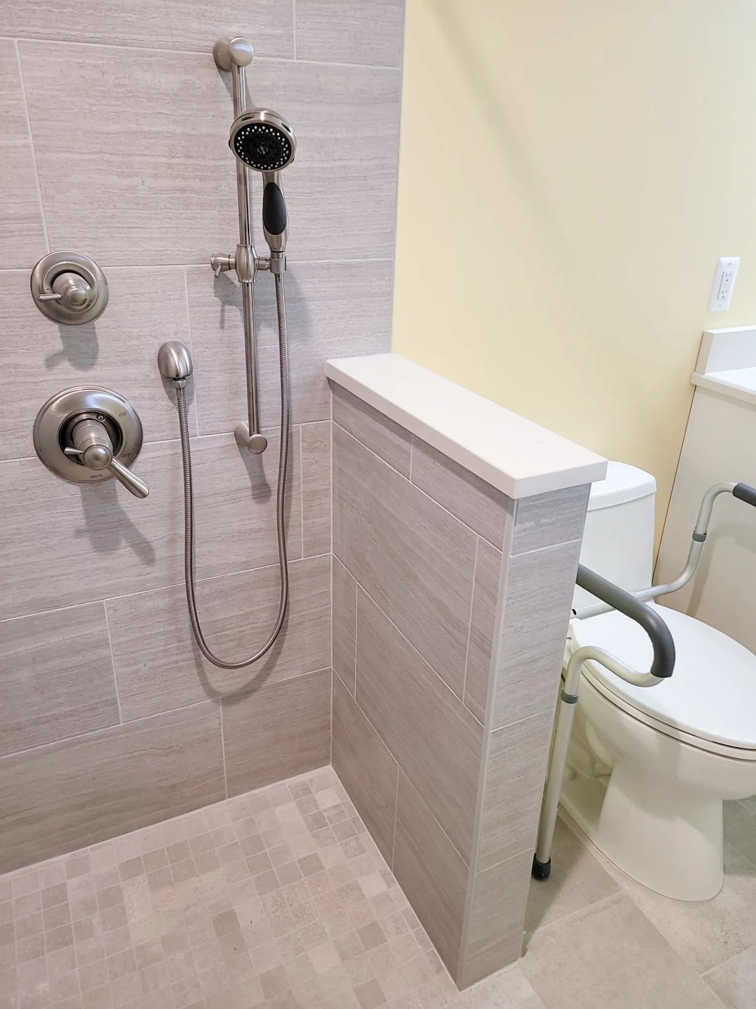 modern bathroom with gray tile shower, handheld showerhead, and accessible toilet