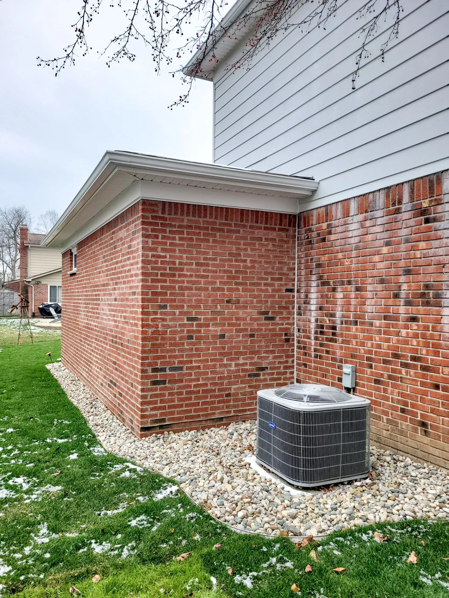 Exterior view of a brick house corner with an air conditioning unit, surrounded by pebbles and green grass