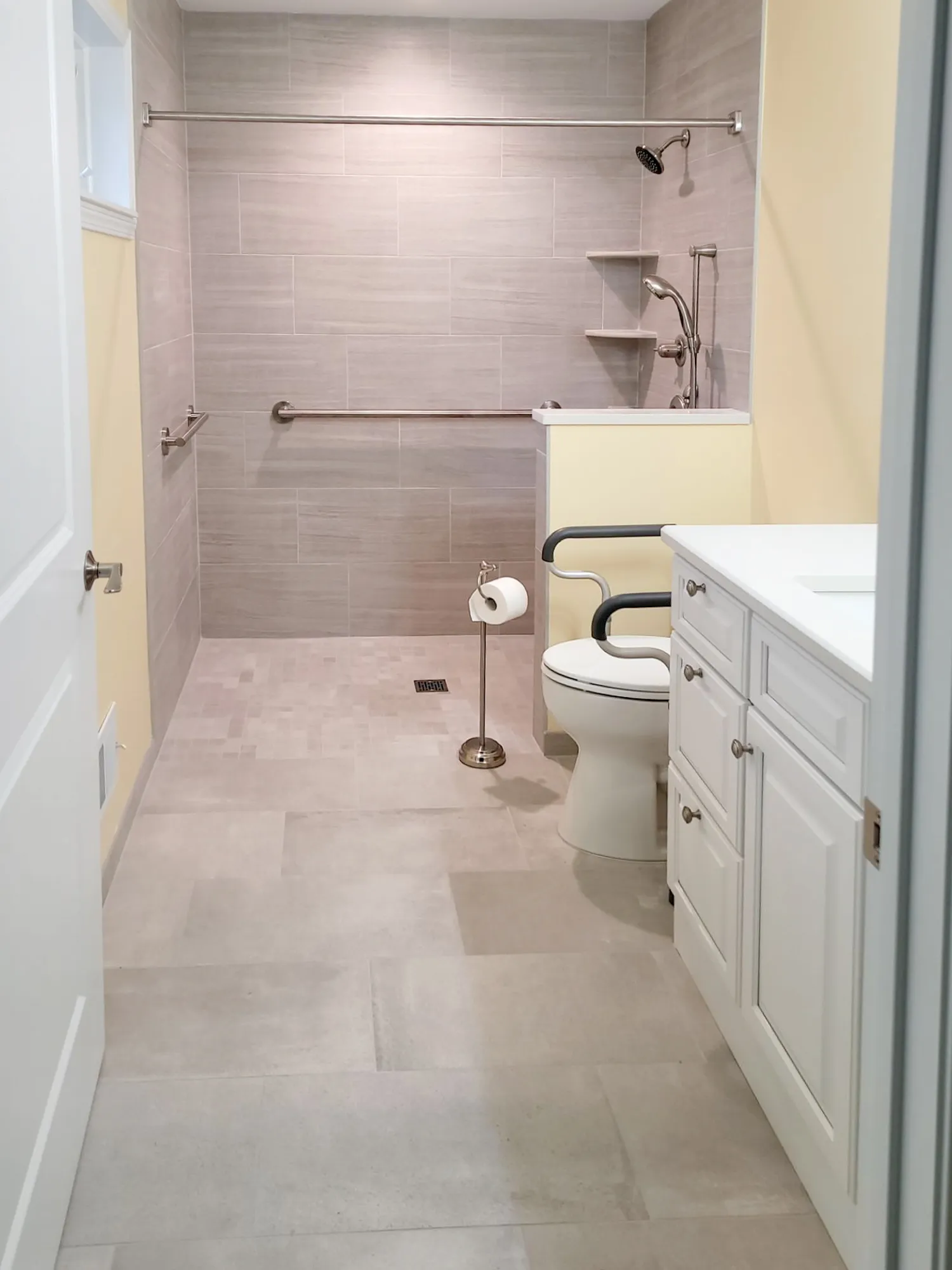 Accessible modern bathroom featuring beige tile, white cabinetry, grab bars, and minimalist design.