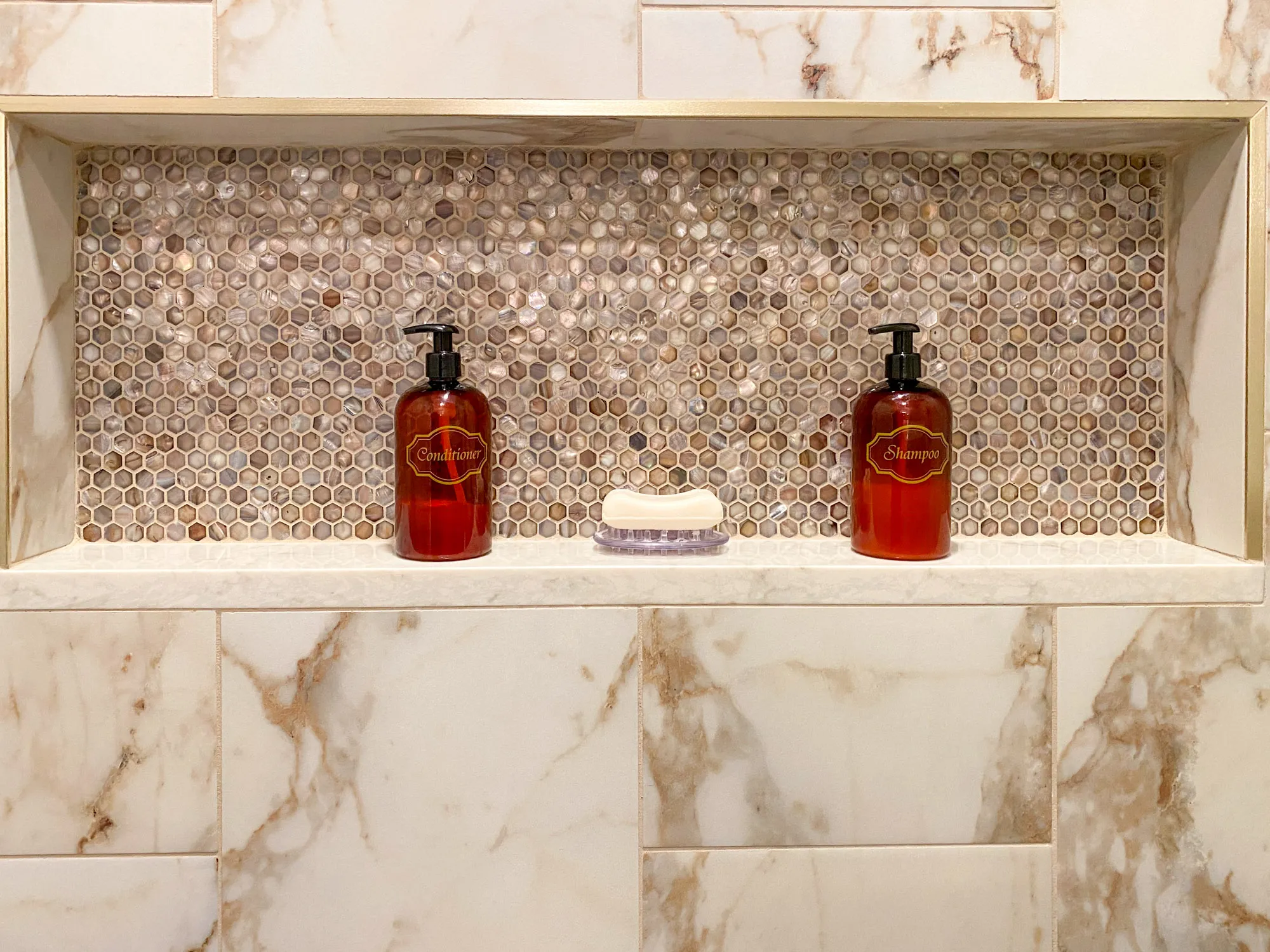 Luxury bathroom with marble tiles, hexagon mosaic backsplash, and shampoo and conditioner dispensers