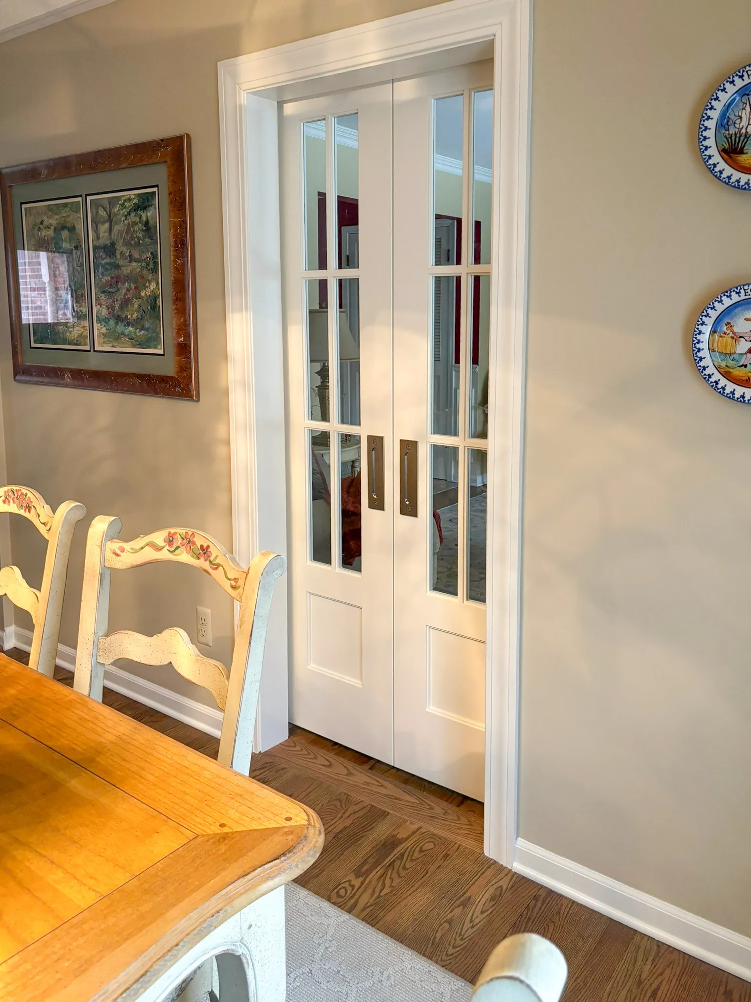 Elegant dining area featuring a rustic wood table, floral chairs, and a set of glass-paned doors leading to another room.