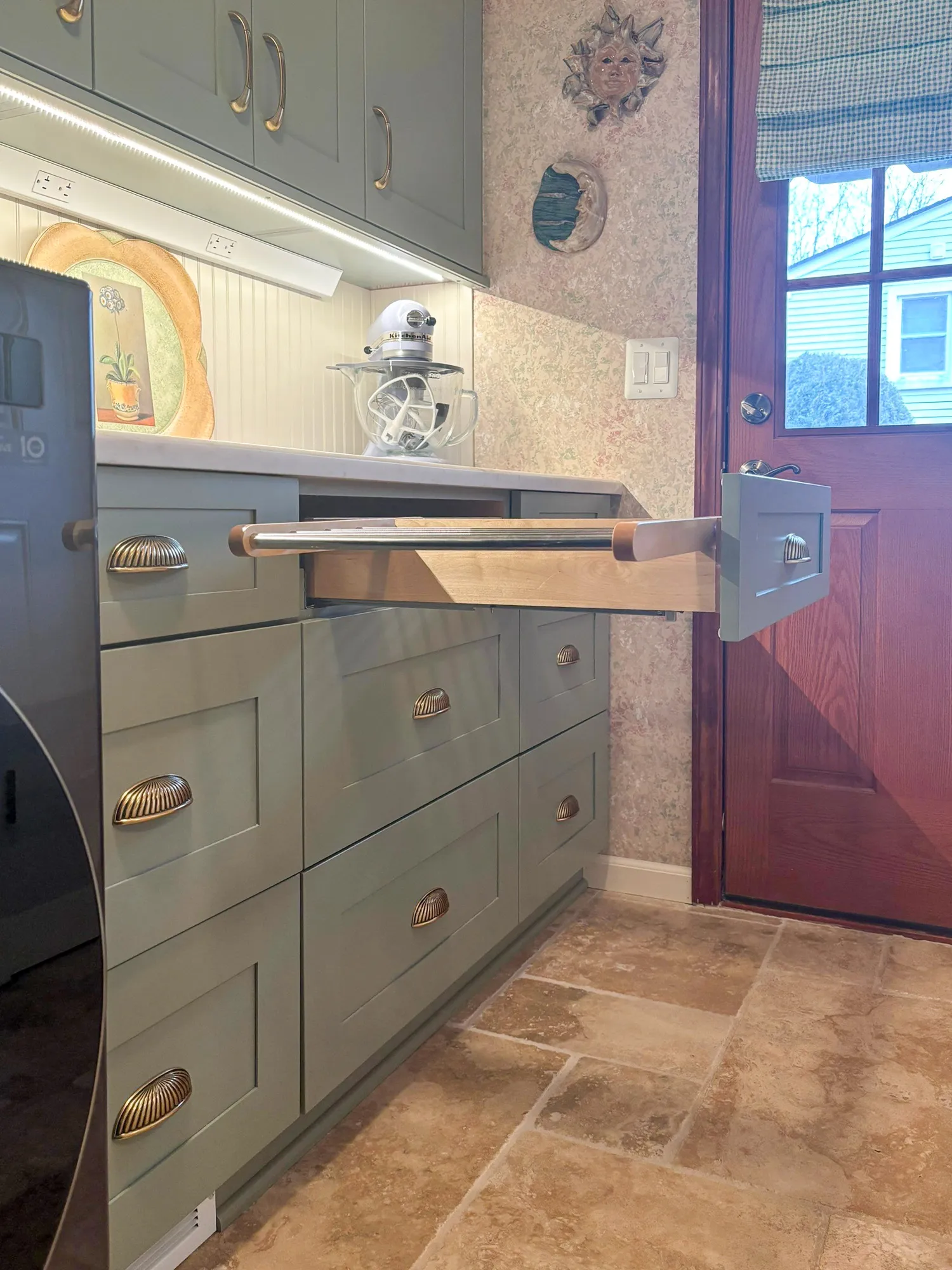 Contemporary kitchen featuring green cabinetry with brass handles, vintage decor, and natural stone flooring.