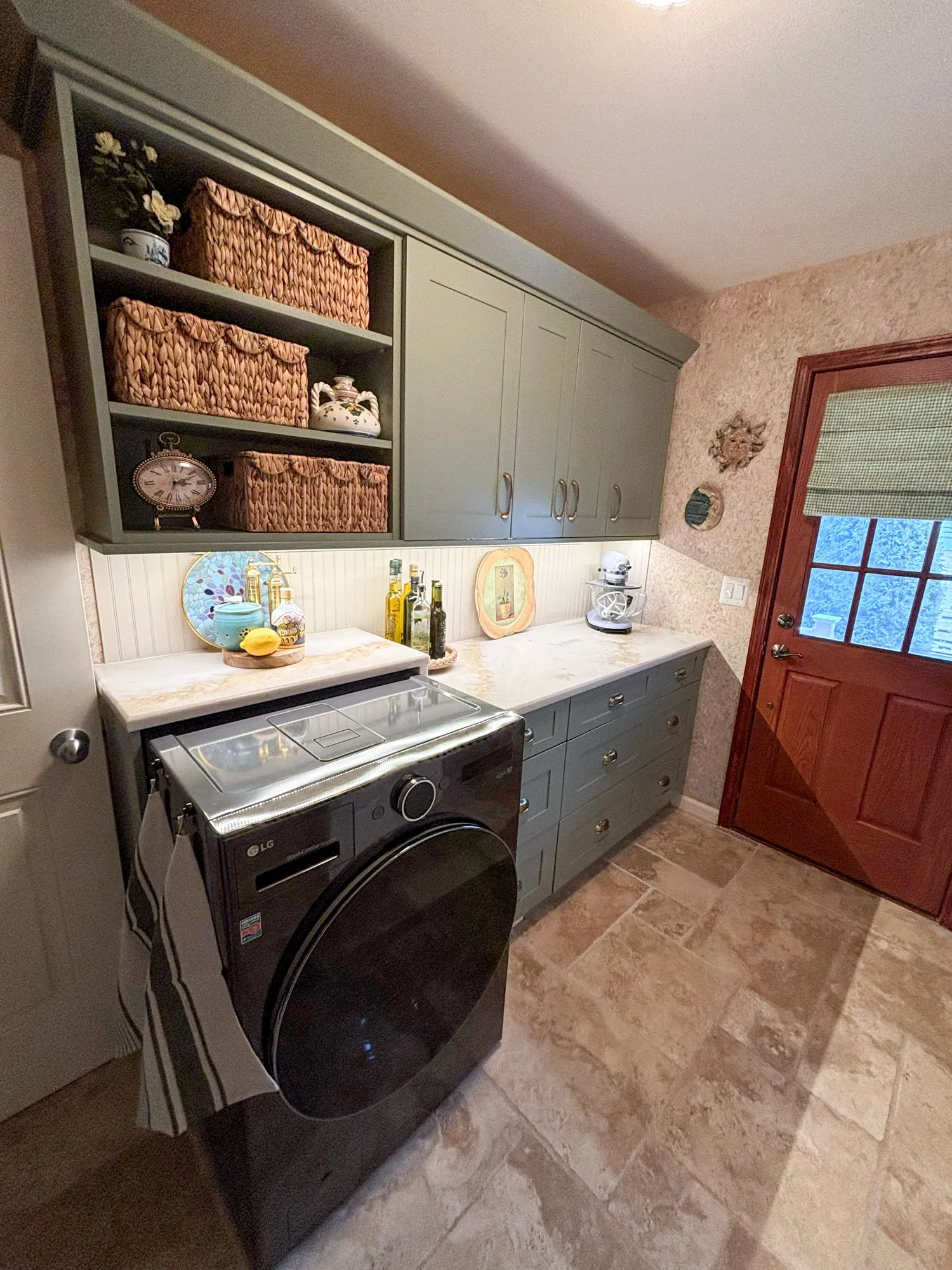 Cozy modern laundry room featuring gray cabinetry, a black LG washer, and decorative baskets.