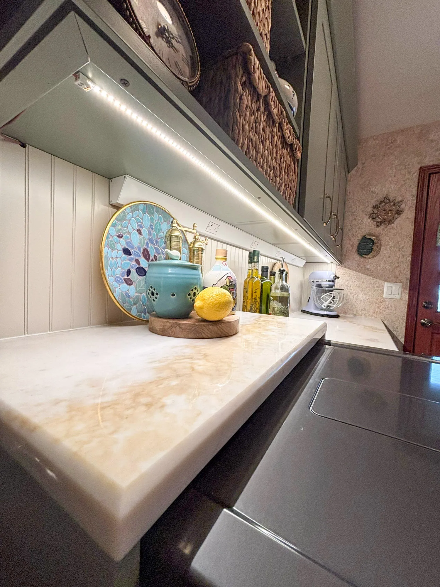 Contemporary kitchen countertop with marble surface and decorative items, featuring a blue teapot and vibrant olive oil bottles