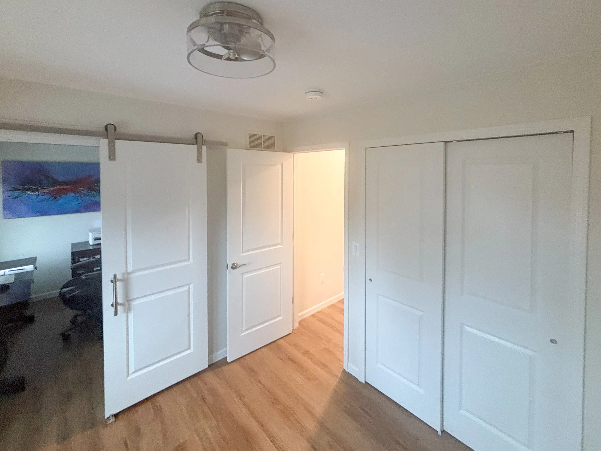 Modern office entry with white doors and wooden floor, featuring a sliding barn door in a contemporary design.