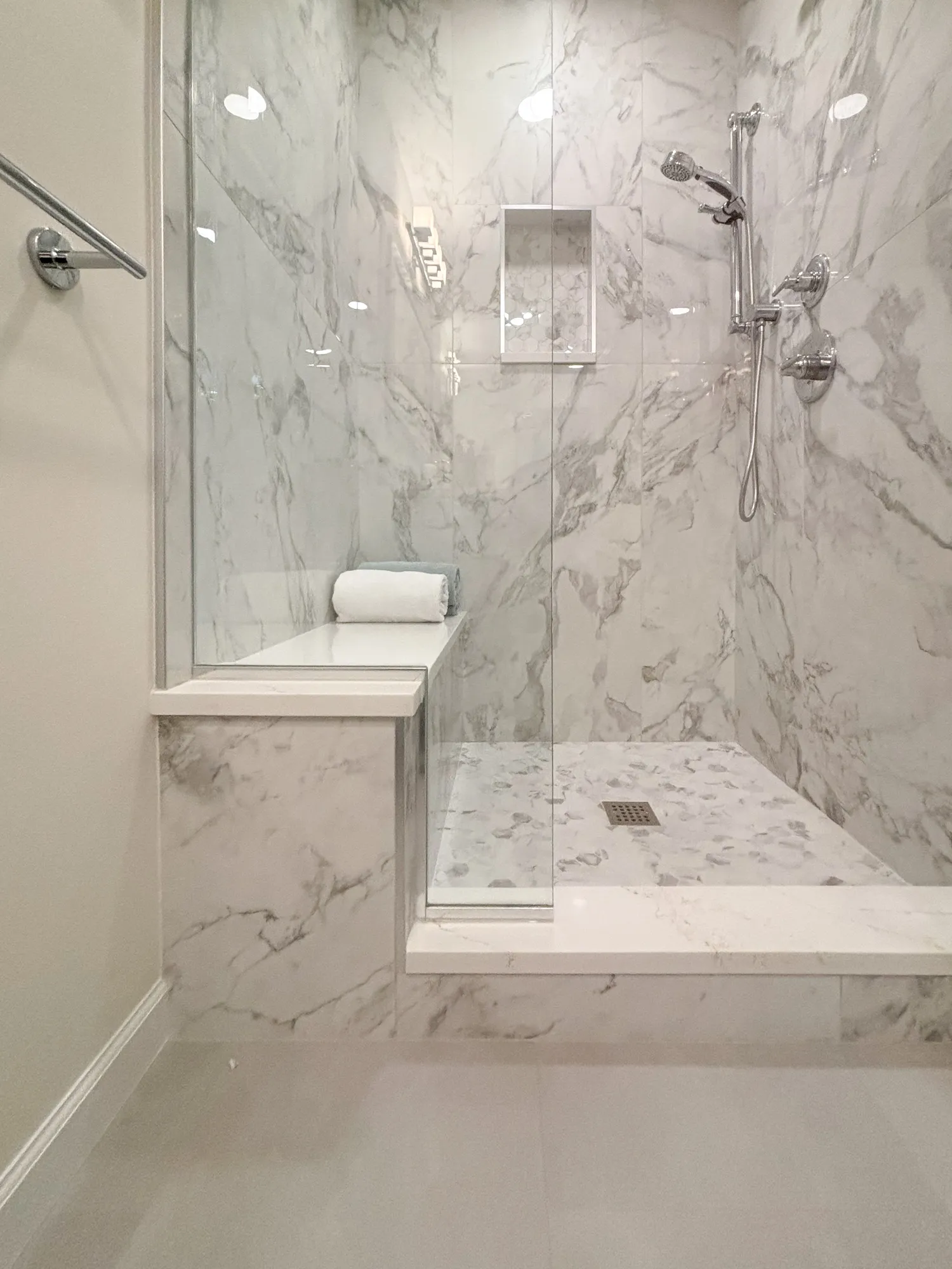 Luxury bathroom shower featuring elegant marble walls and a bench with chrome fixtures