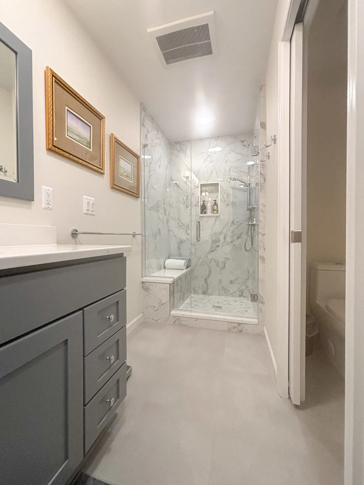 Stylish modern bathroom featuring gray cabinetry and a glass shower, decorated with marble tiles.