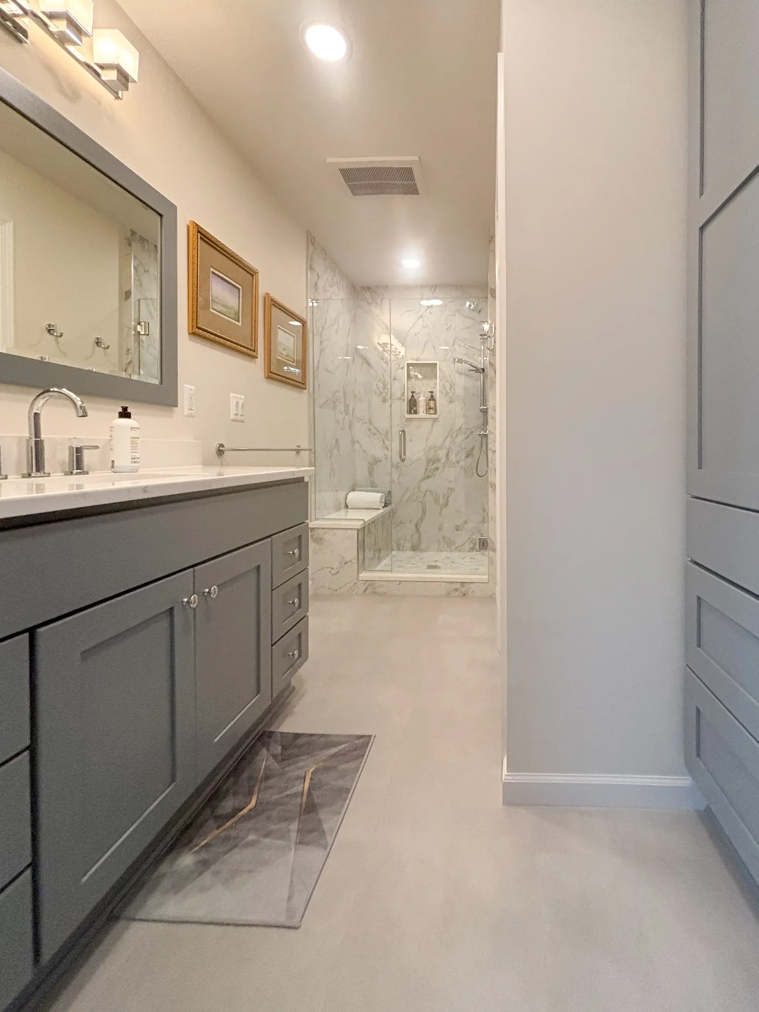 Modern bathroom featuring grey cabinetry, marble shower, and elegant light fixtures.