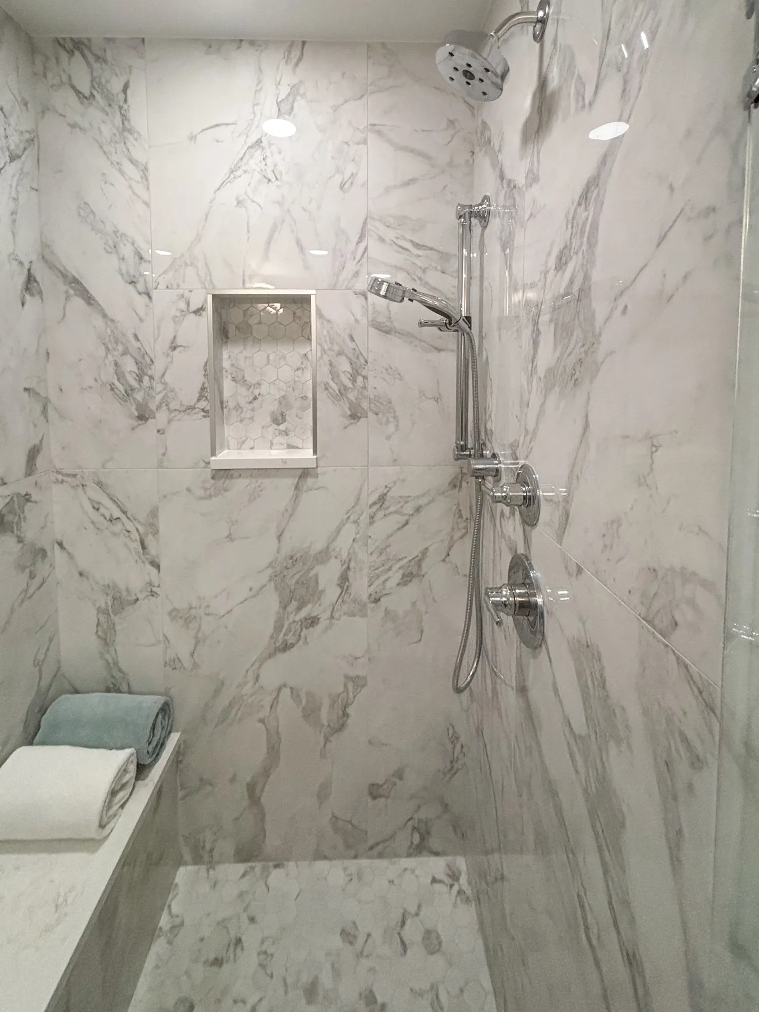 Luxury bathroom with marble shower and hexagon tile, featuring a built-in shelf for toiletries.