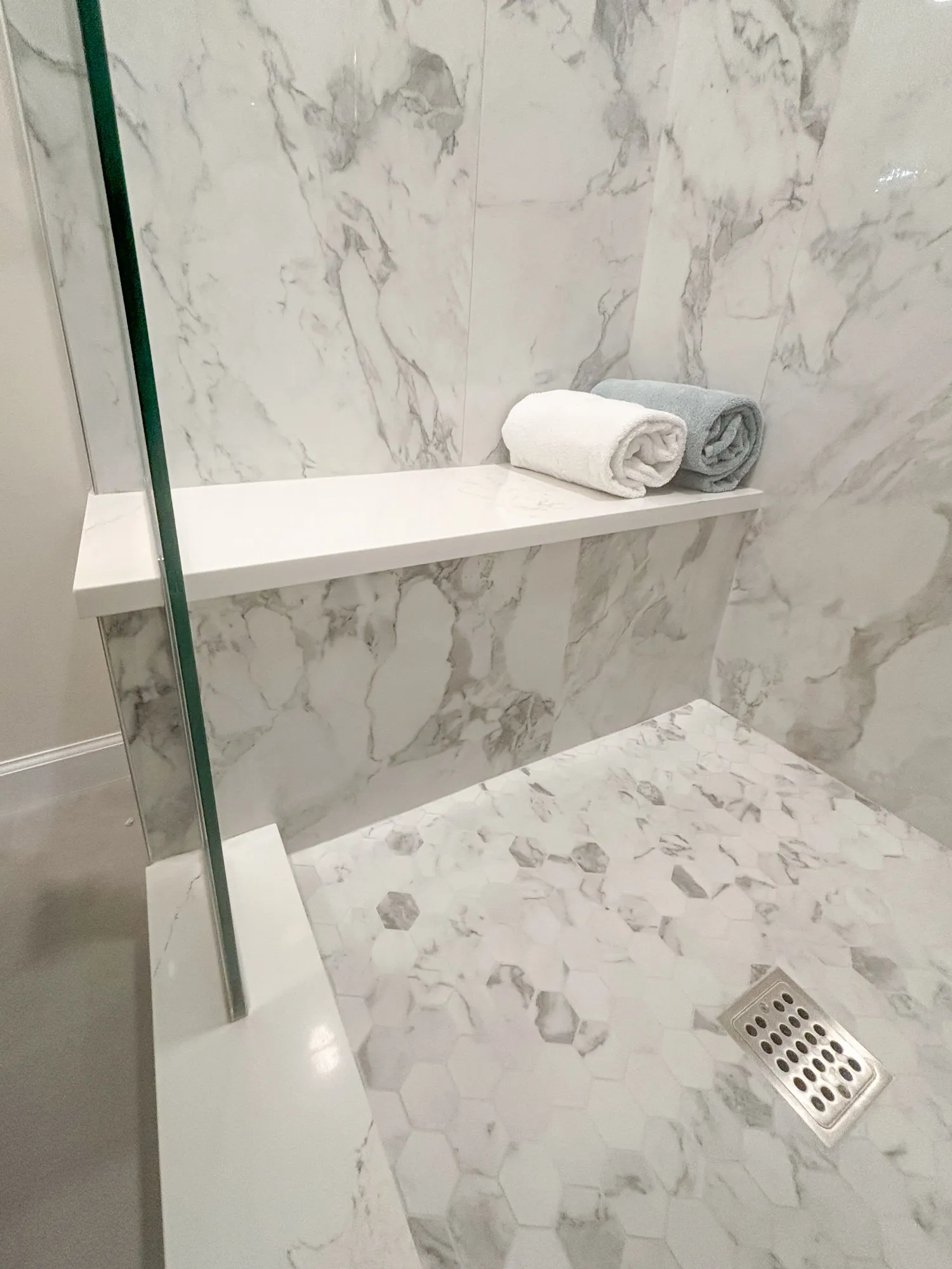 Luxury bathroom shower with marble walls and hexagonal tile flooring, featuring towels neatly arranged.