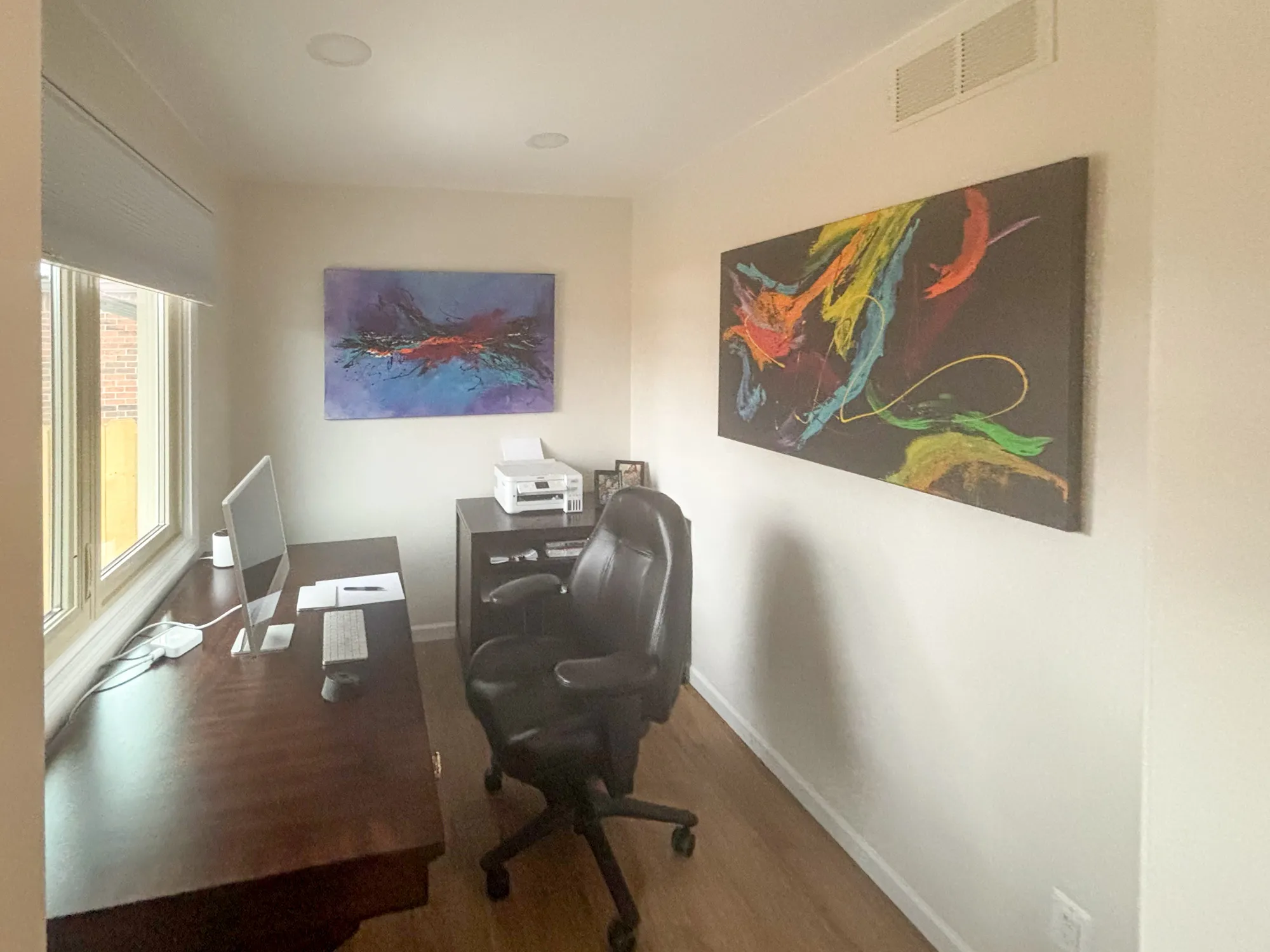 Modern home office with colorful abstract art, brown desk, and large windows