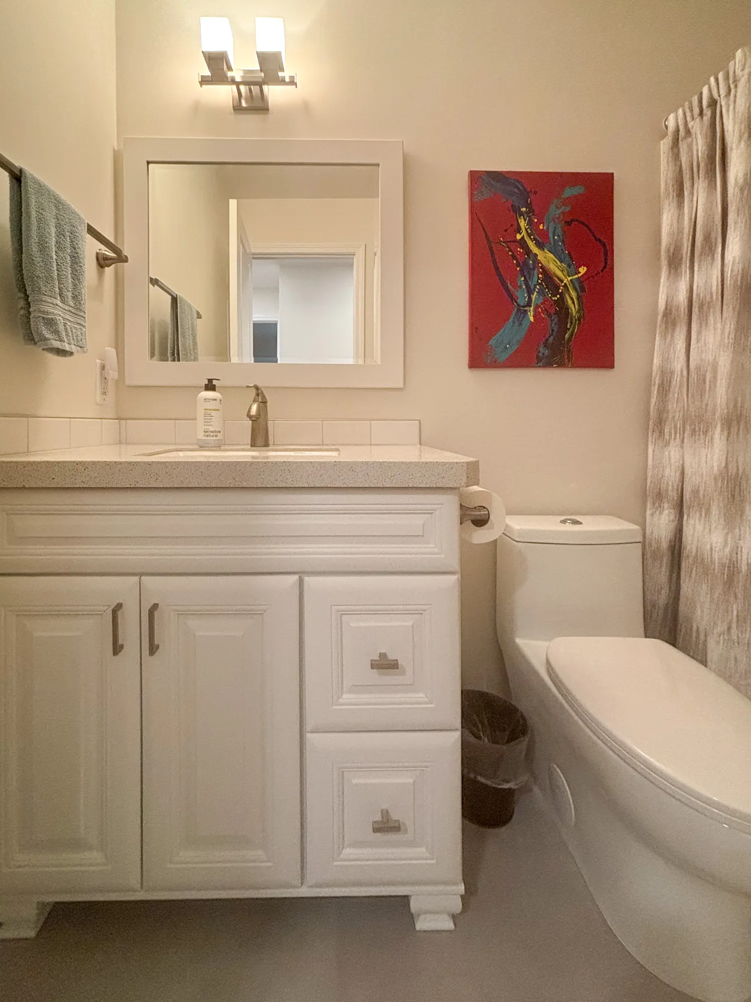 Modern bathroom featuring a white vanity with a mirror, light fixture, and colorful artwork.