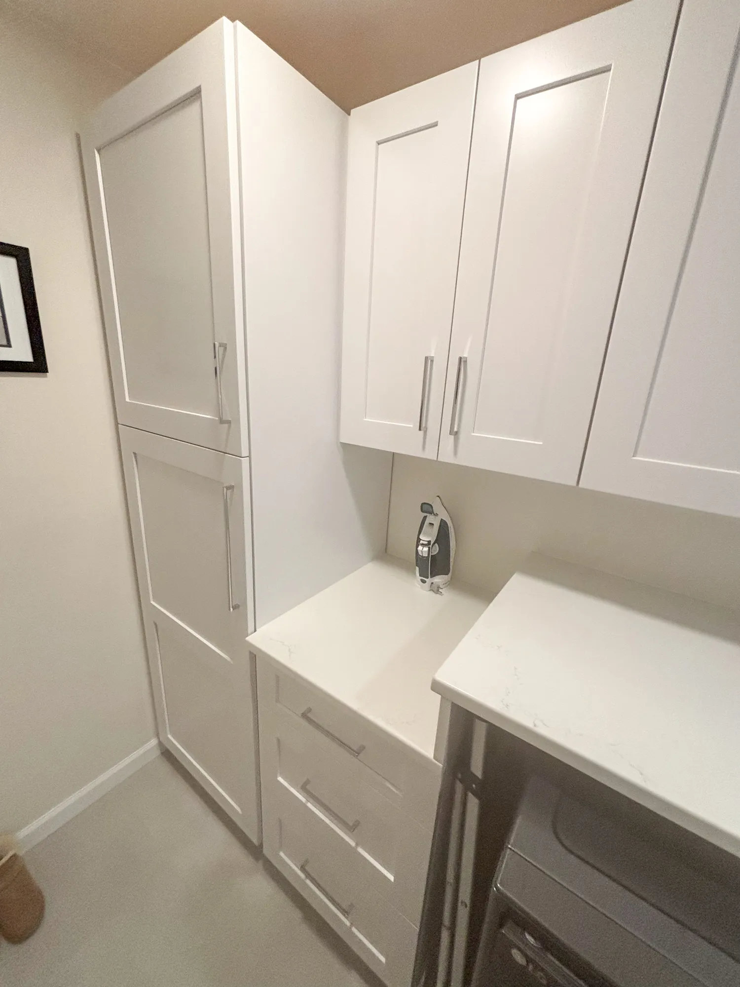 Modern laundry room with white cabinetry, quartz countertop, and an iron located in a small space.