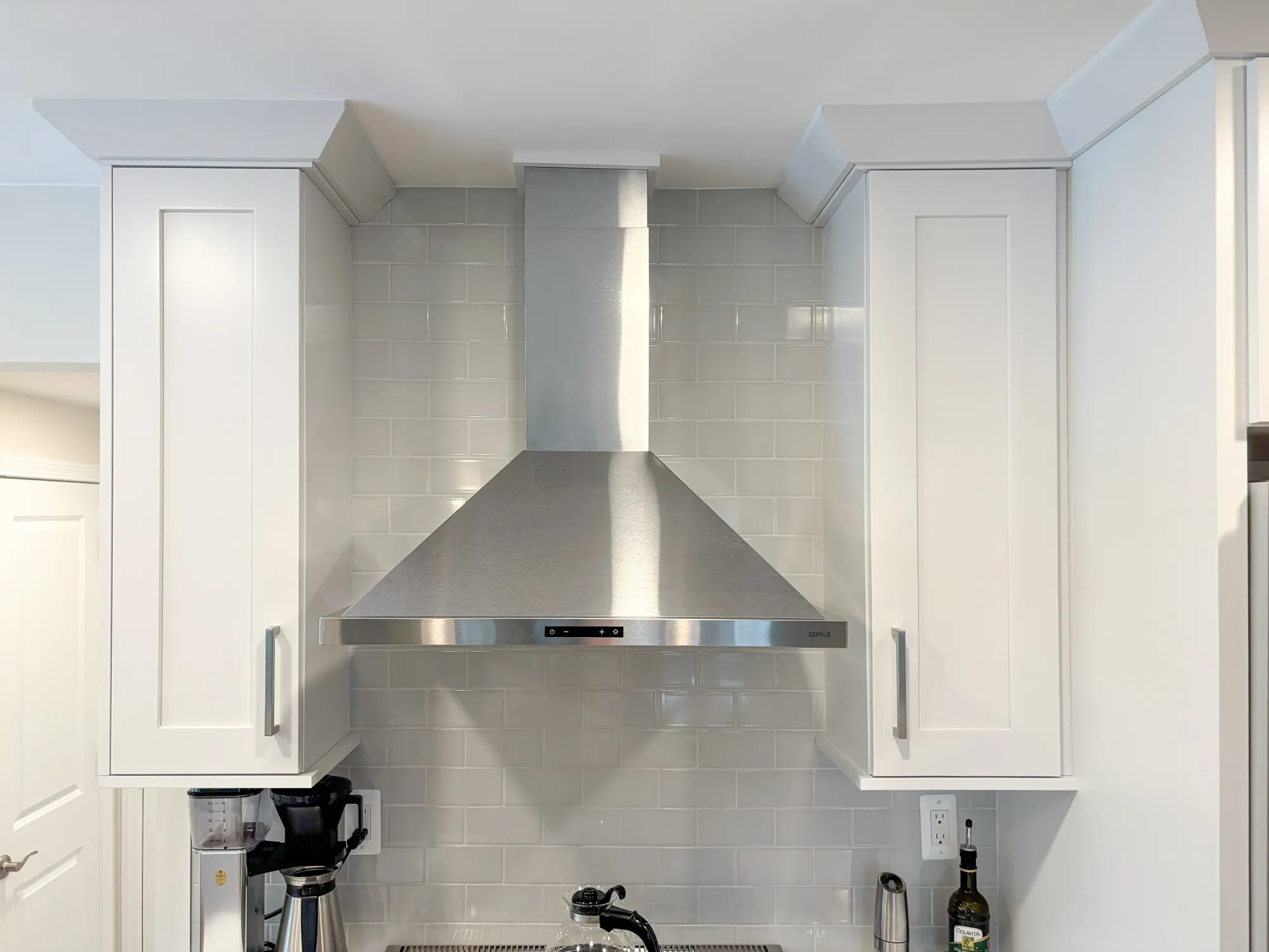 modern kitchen featuring white cabinetry, stainless steel range hood, and gray subway tile backsplash