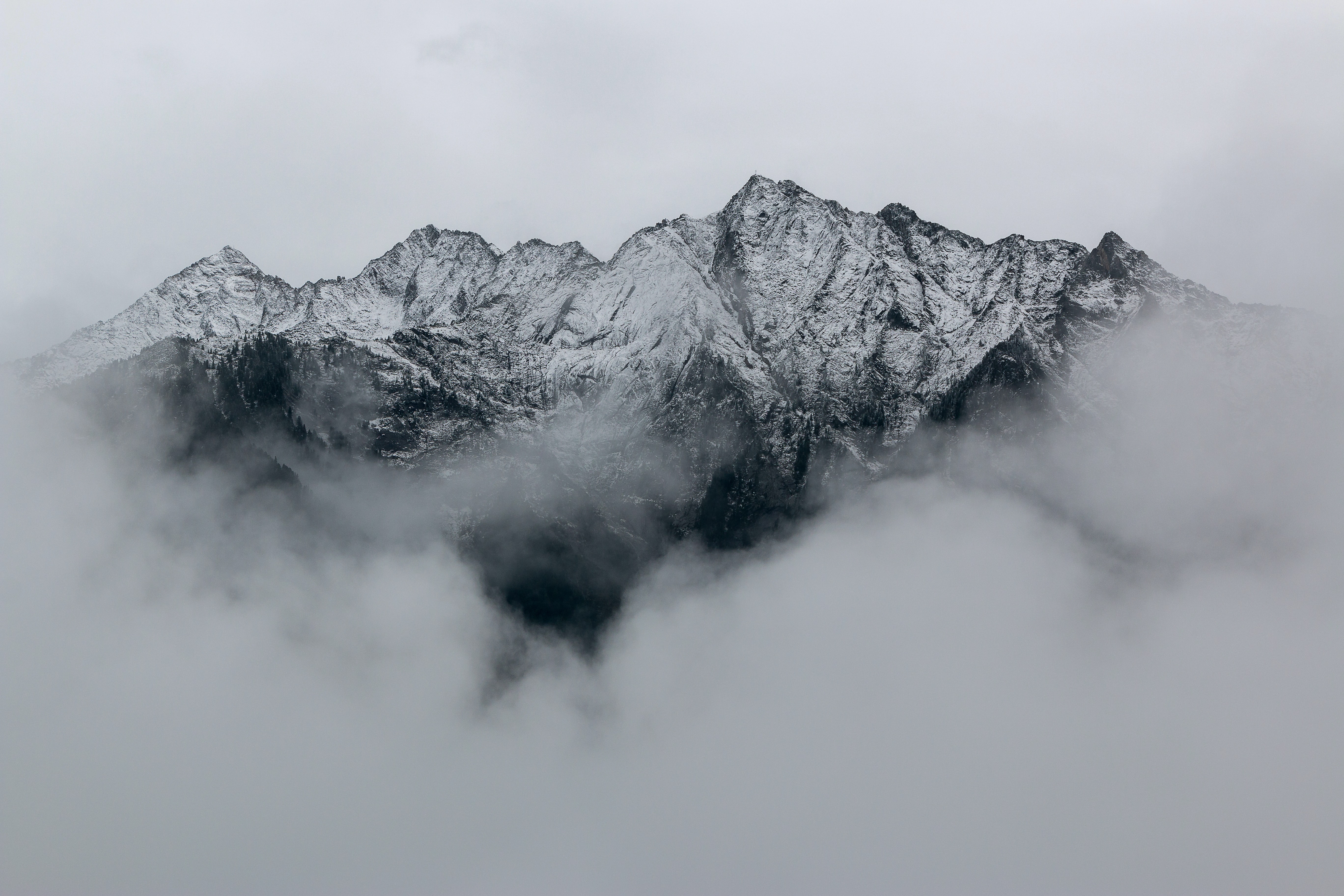 Snow-covered mountain peaks partially obscured by mist and clouds under a gray sky.