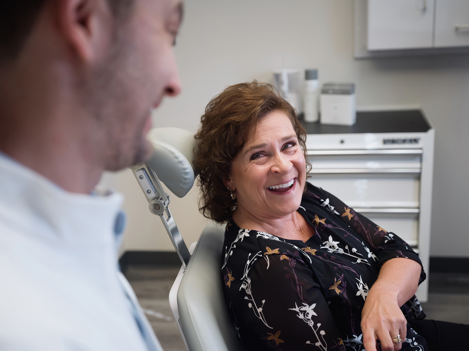 Smiling woman sitting in a dental chair talking to a male dentist in a clinic.