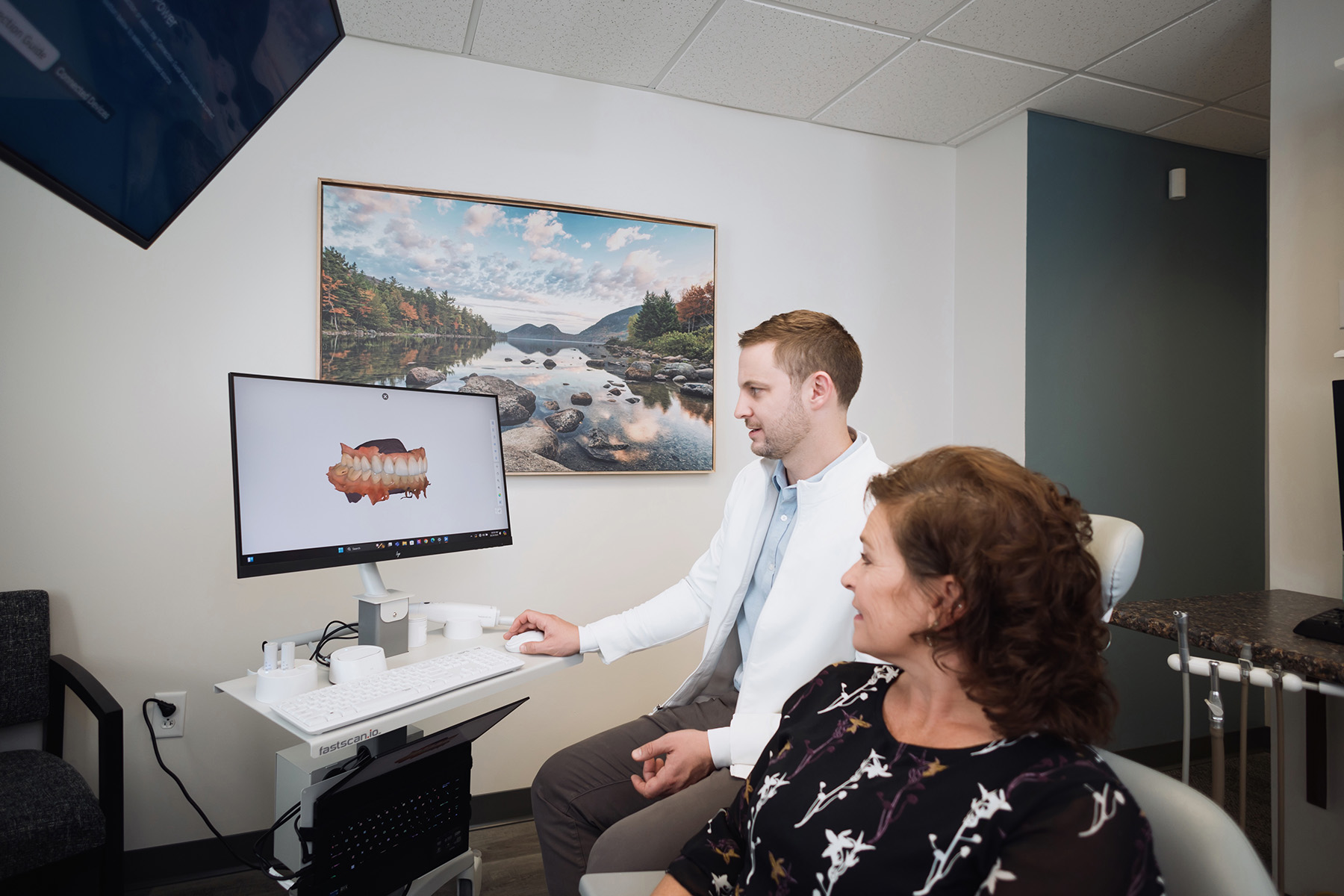 Dentist showing a 3D digital dental model on a computer screen to a female patient in a consultation room.