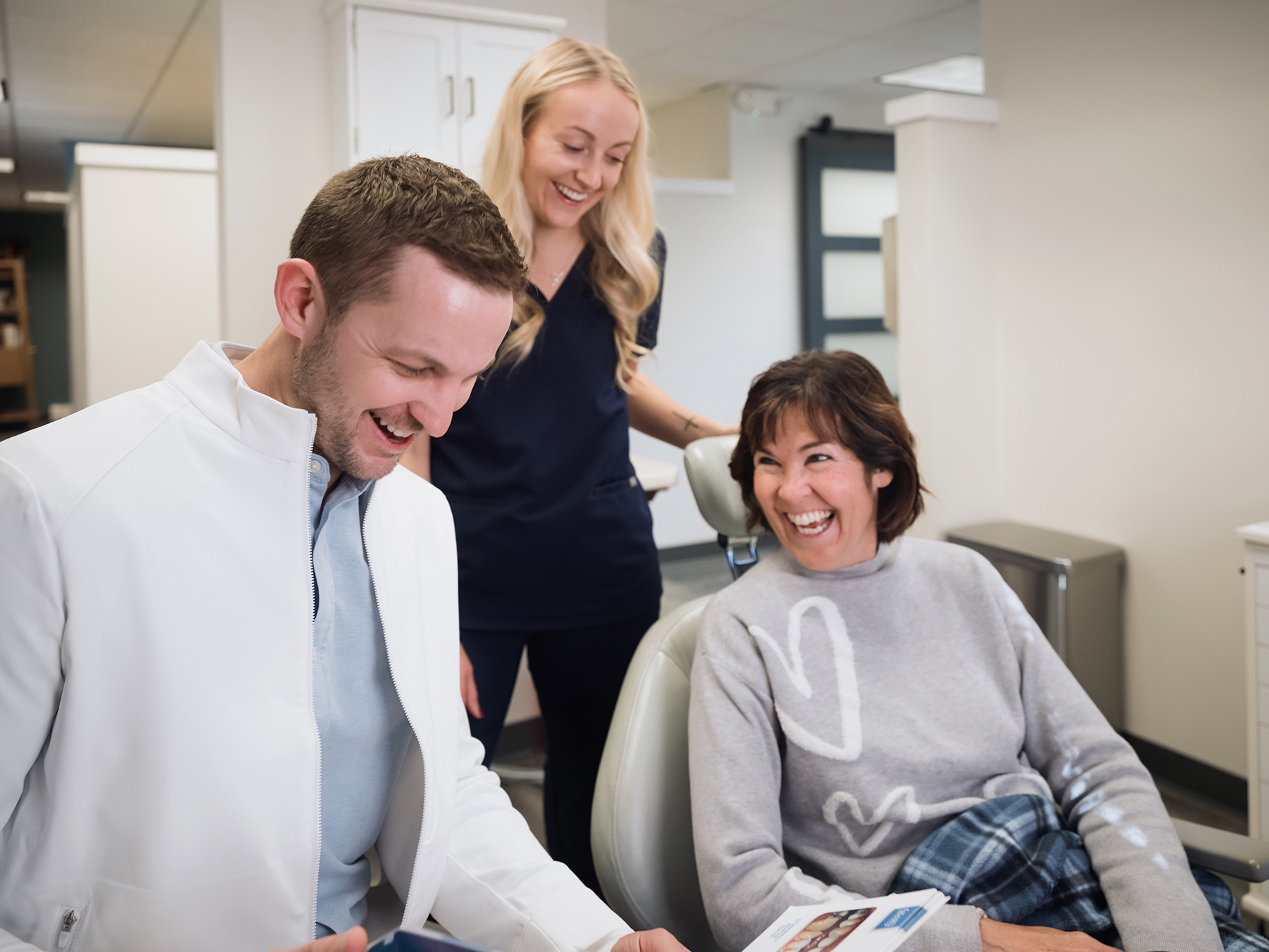 A dentist, patient, and dental assistant smiling and laughing together in a dental clinic.