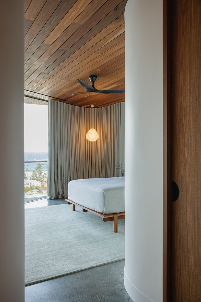 Master bedroom with ocean view and curved curtain track with tall grey curtains, a black fan and a hanging feature light