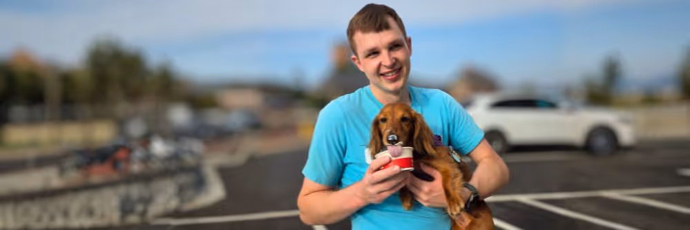 Doo Away owner smiling while holding small brown Dachshund dog licking ice-cream from Western Springs Oberweis Dairy cup