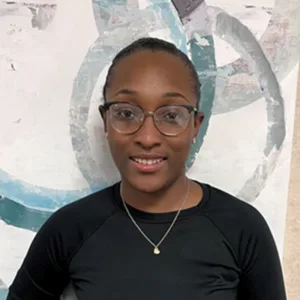 Smiling woman with glasses and a black top standing in front of an abstract painting.
