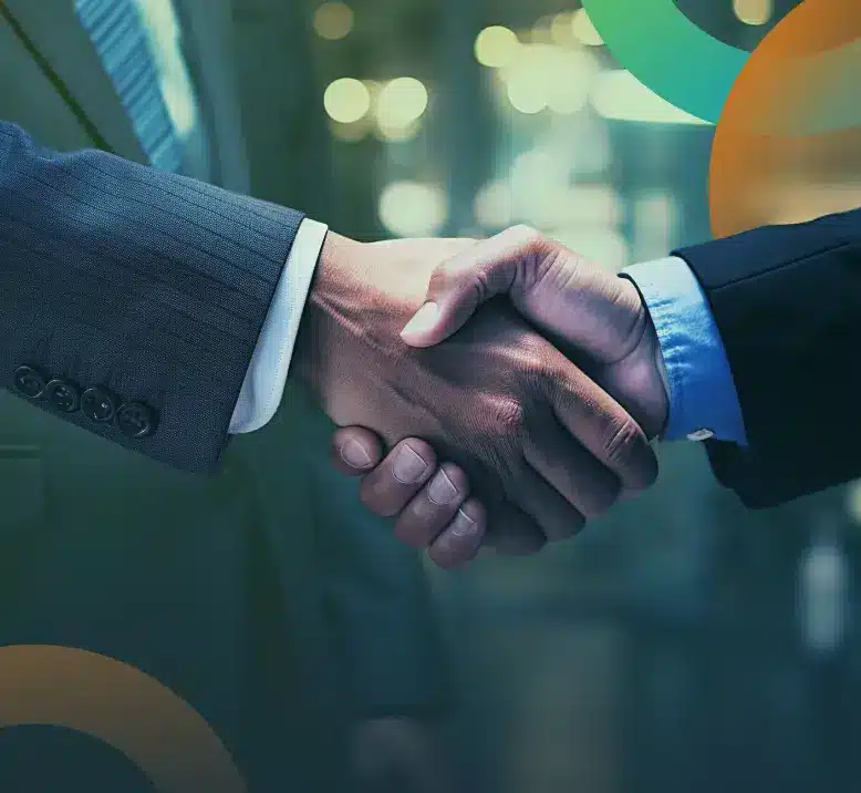 Close-up of two people shaking hands. Both are wearing formal business attire—a suit. The background is blurred, featuring what appears to be office lights and abstract circles in varying shades of green, blue, and orange.