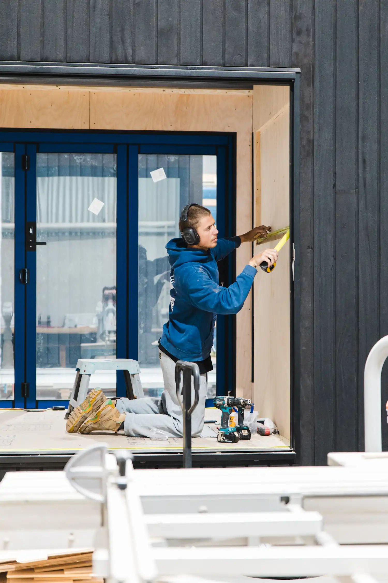 Construction worker wearing ear protection measuring a wooden wall inside a tiny home under construction.