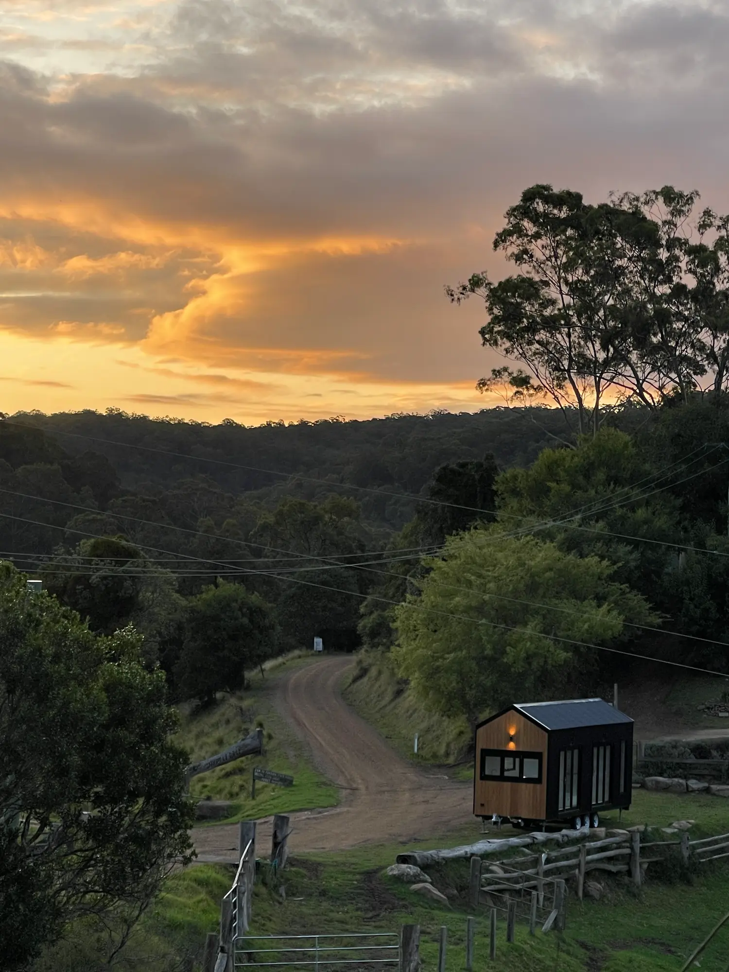 Brown, timber Tiny Home in field surround by trees with sunset