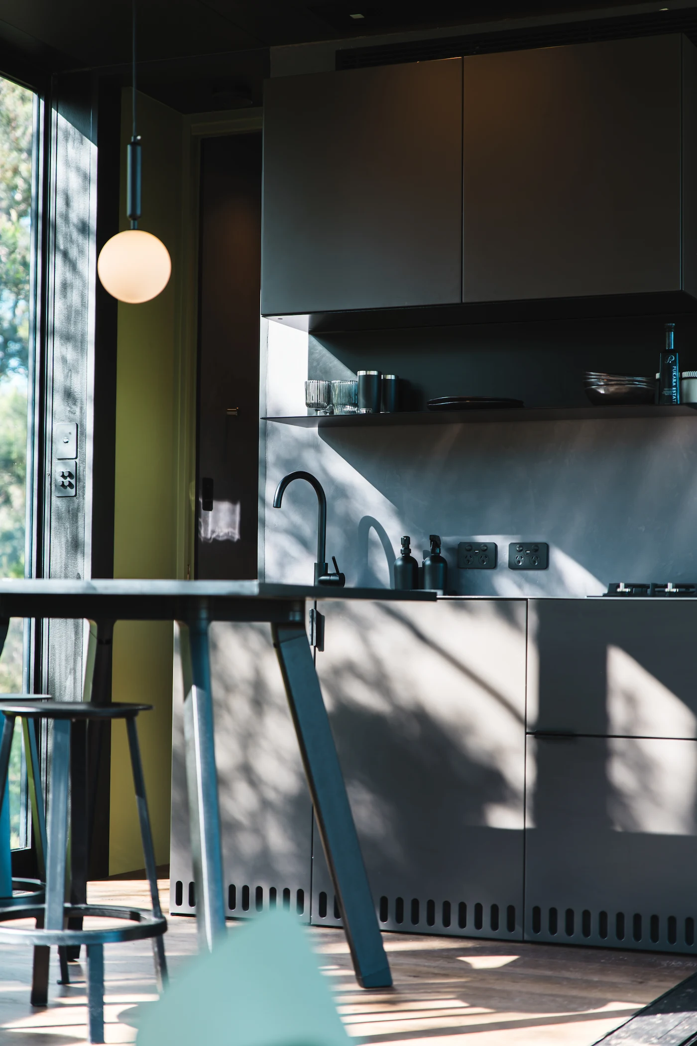 Modern kitchen in tiny home with black cabinets, a black faucet, and sunlight casting shadows through a window onto the cabinets and floor.