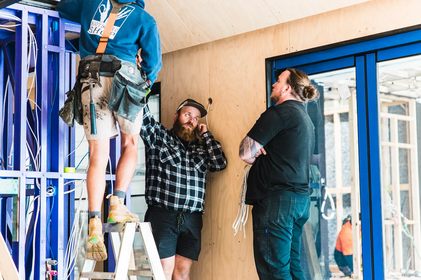 Three Big Fig workers installing wiring and drywall inside a building under construction.