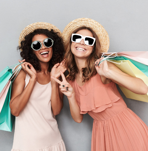 Two friends in sun hats and sunglasses laughing with shopping bags