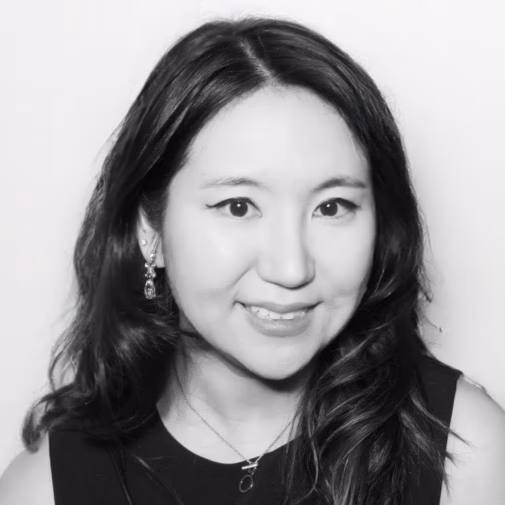 Black and white portrait of Michelle Ma, a smiling woman with long dark hair, wearing earrings and a necklace.
