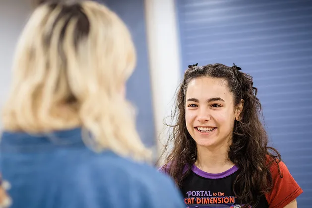 Smiling young woman with dark curly hair engaging in conversation with a blonde person.
