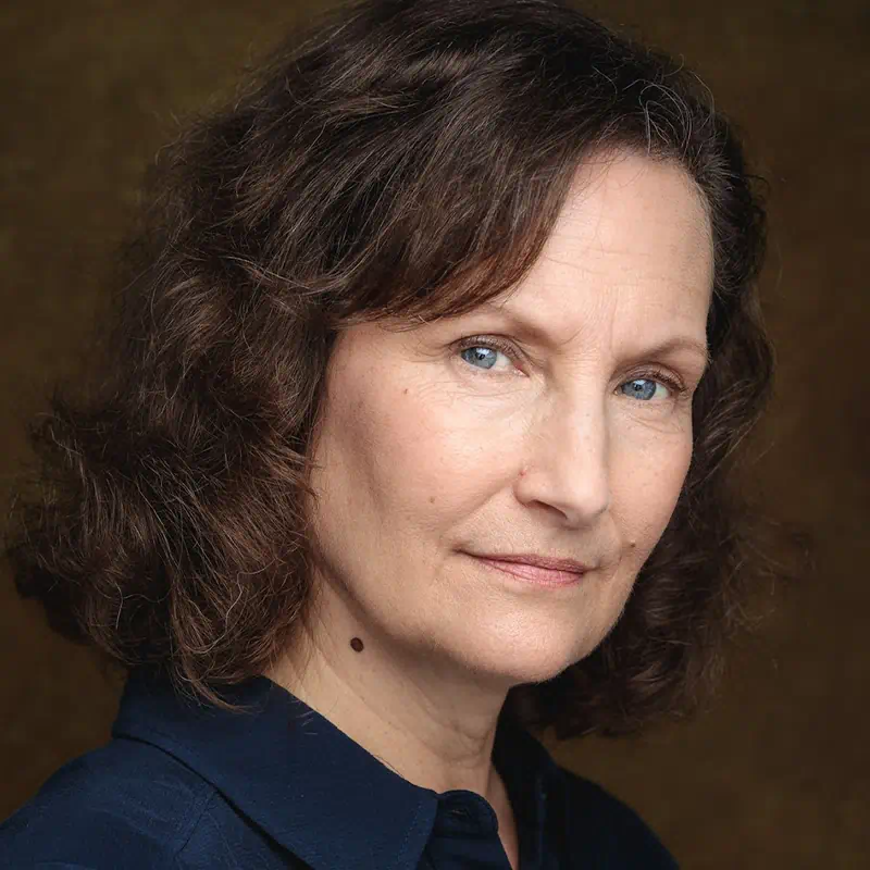 Portrait of a middle-aged woman with curly brown hair and blue eyes wearing a navy blue shirt, looking at the camera.