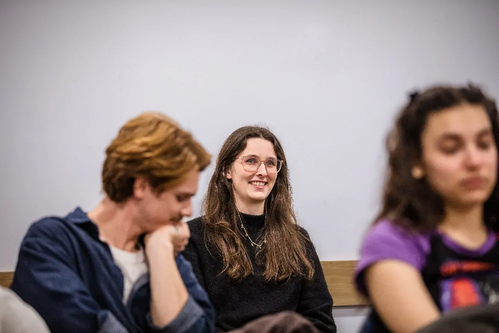 Three young adults sitting indoors with a smiling woman with glasses in the center.