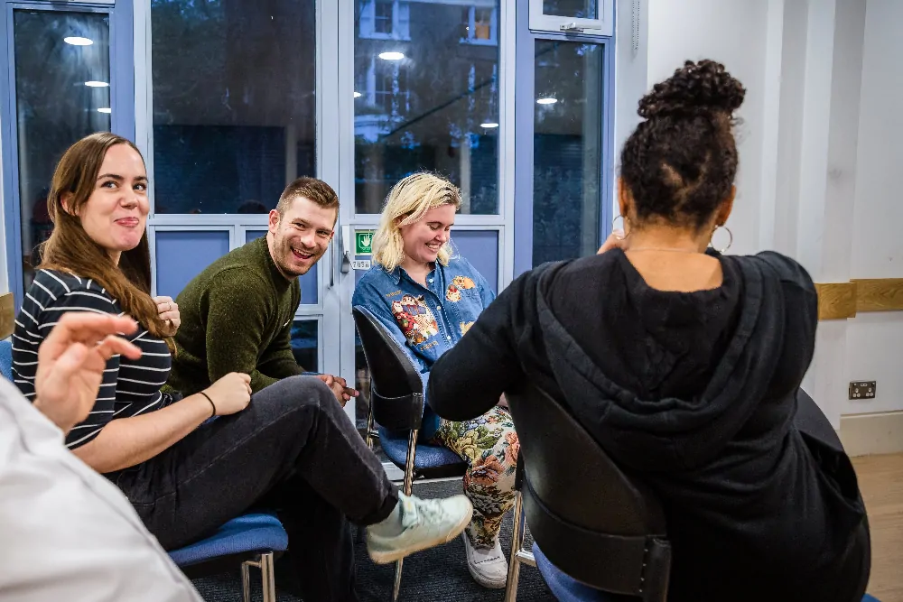 Group of four people sitting in a circle in a room, engaged in a lively conversation with smiles and laughter.