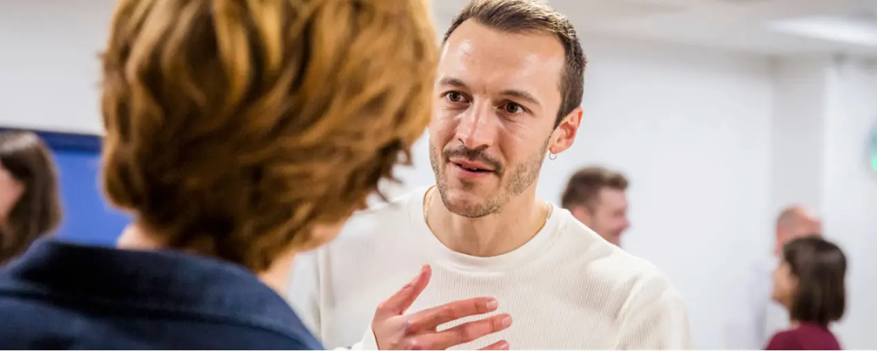 Man in white shirt speaking to a woman with short brown hair in a social setting.
