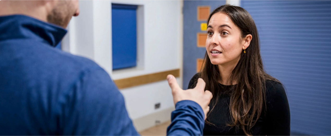 Woman attentively listening to a man speaking and gesturing with his hand indoors.
