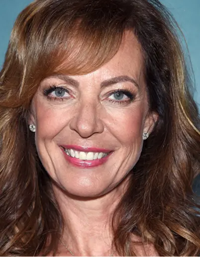 Close-up portrait of a smiling woman with light blue eyes and wavy brown hair.