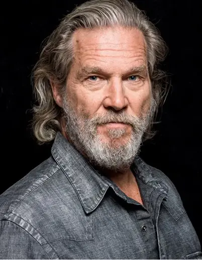 Portrait of an older man with gray hair and beard wearing a gray button-up shirt against a black background.