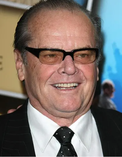 Man with short hair wearing black-framed glasses, a white shirt, black suit, and black tie smiling at an event.