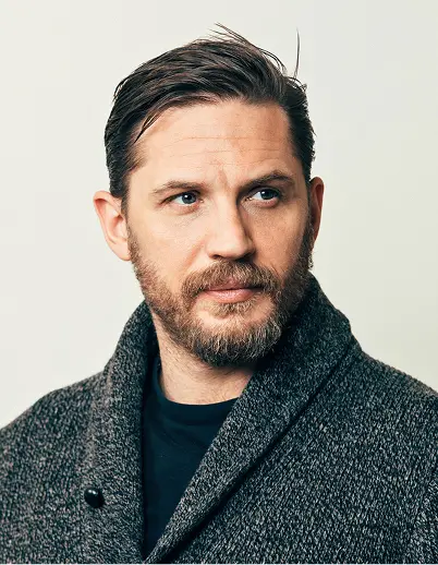 Man with a beard and mustache wearing a dark gray wool coat, looking slightly to the side against a plain light background.