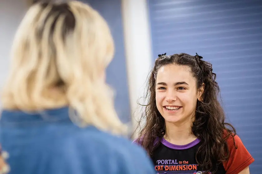 Smiling young woman with curly hair talking to a blonde person with their back to the camera.